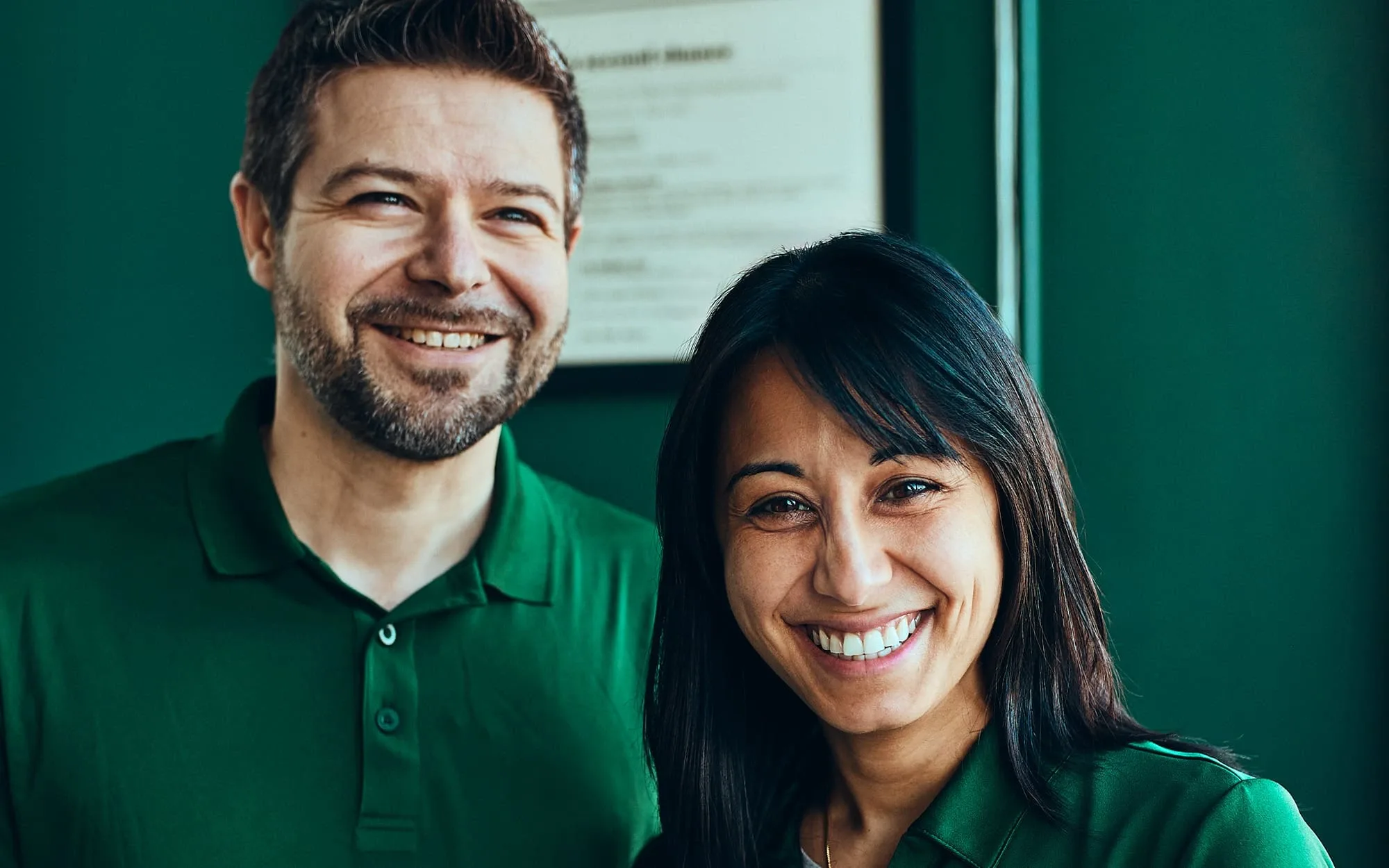 Un homme et une femme en uniforme vert sur un fond vert regarde la caméra avec un sourire